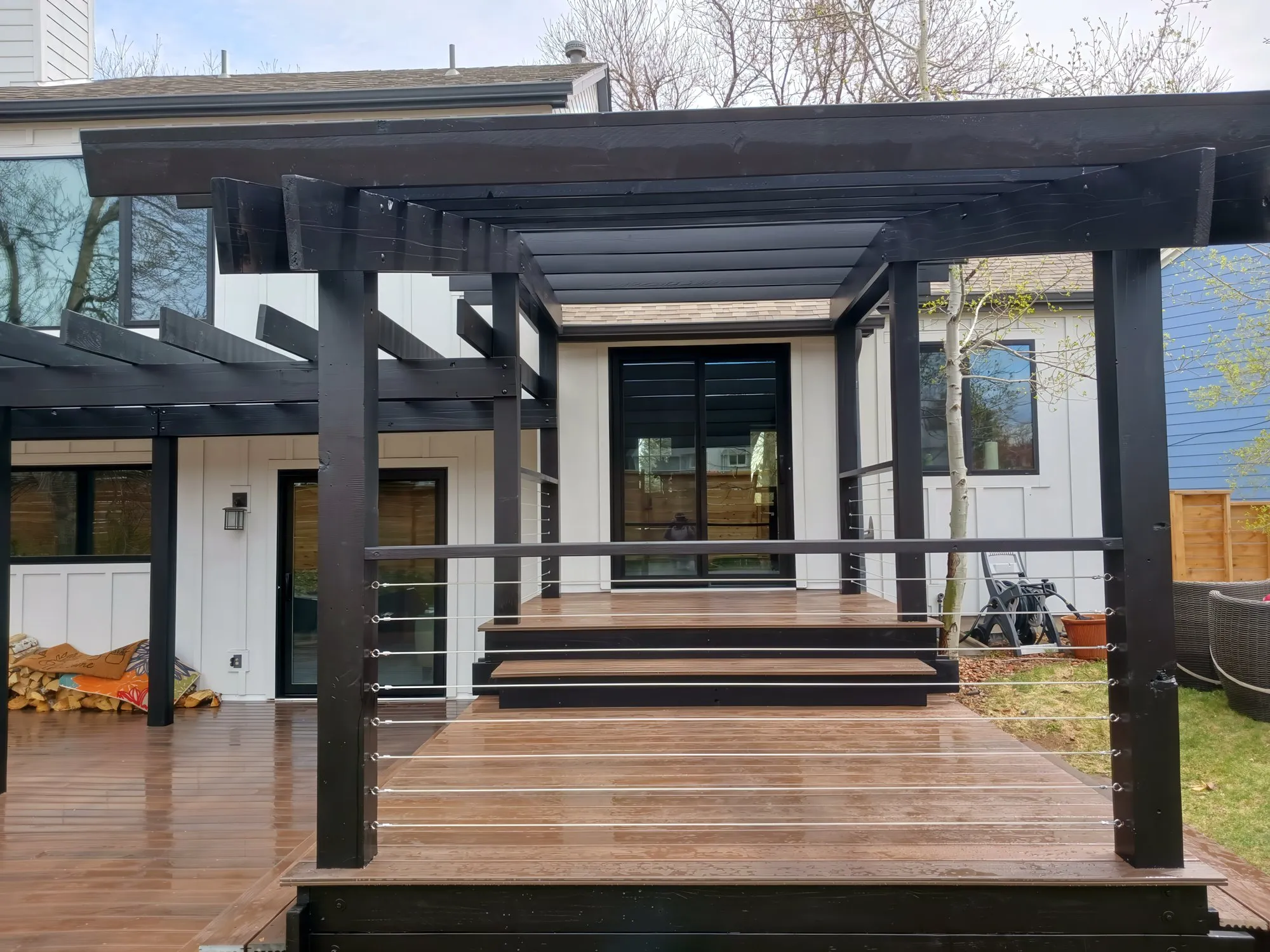 Wood deck with a black pergola and cable railing in front of a modern home