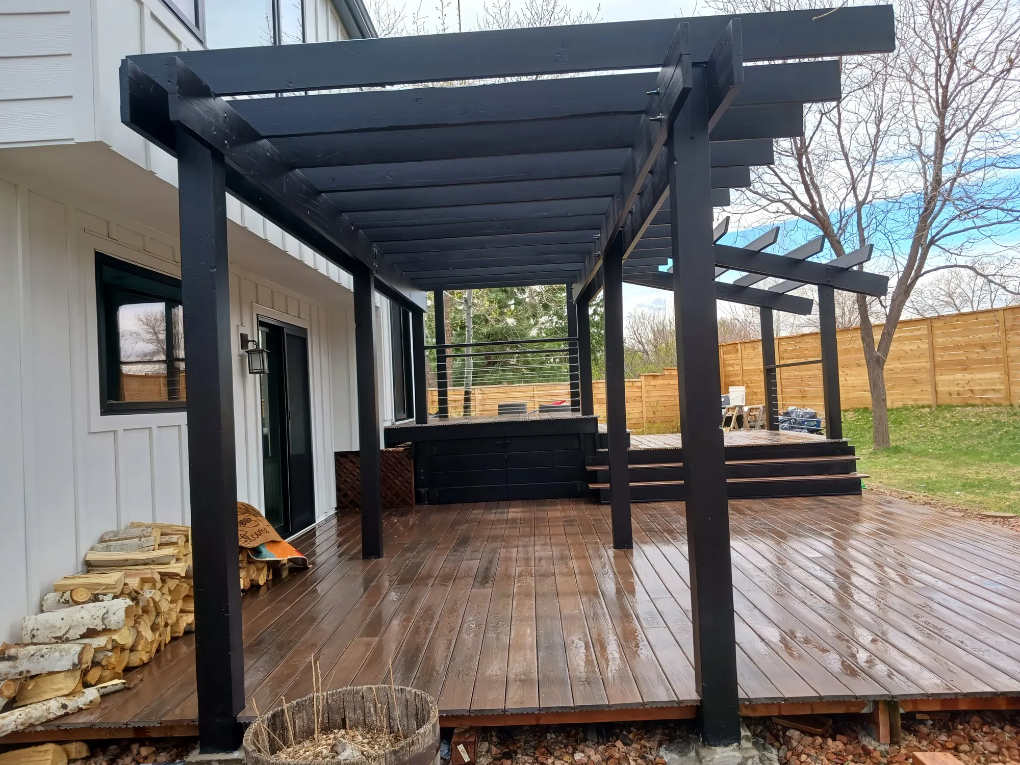 Side view of a wood deck under a black pergola beside a white house