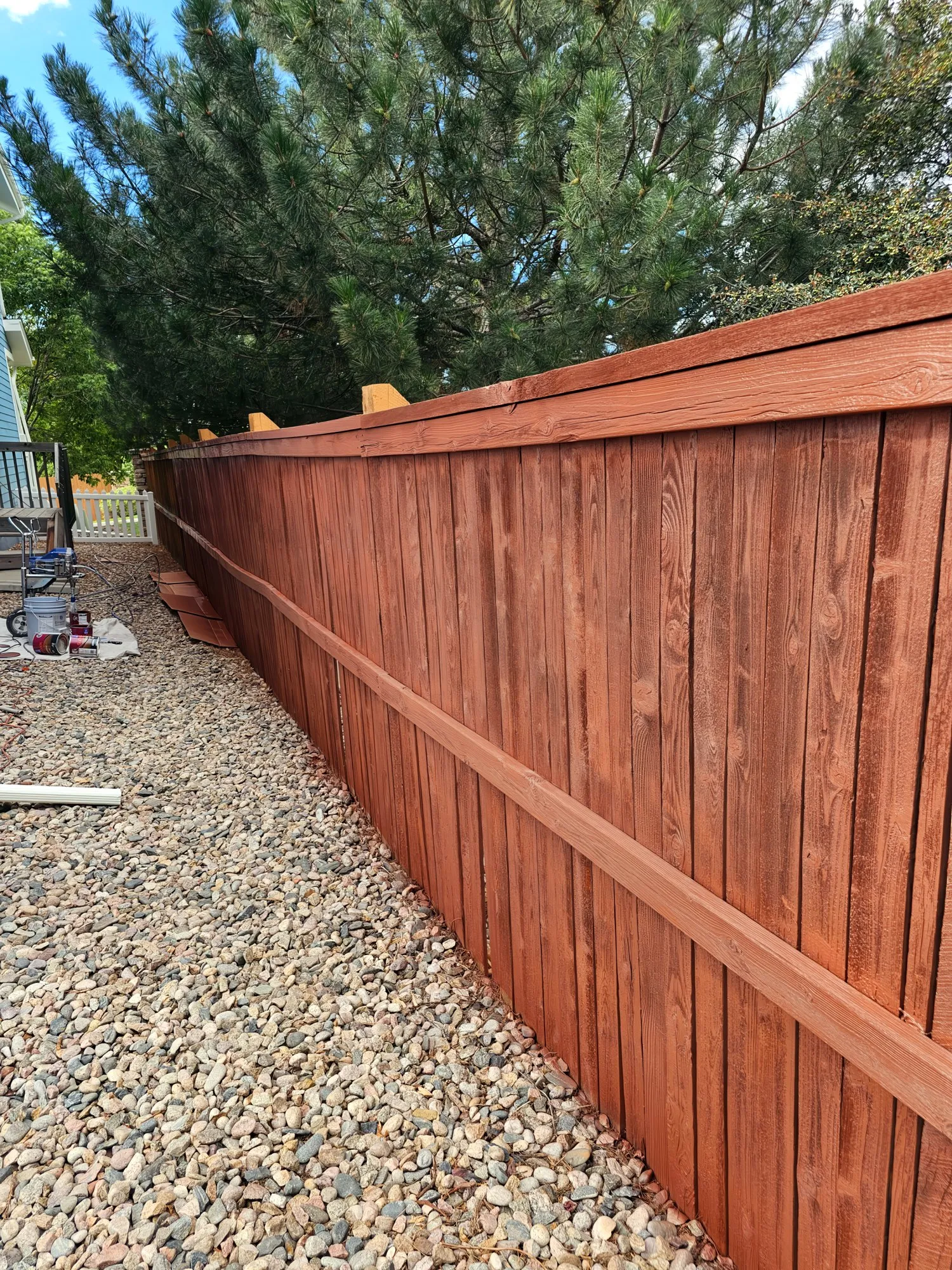 Wood fence with a fresh red-brown stain along a gravel side yard