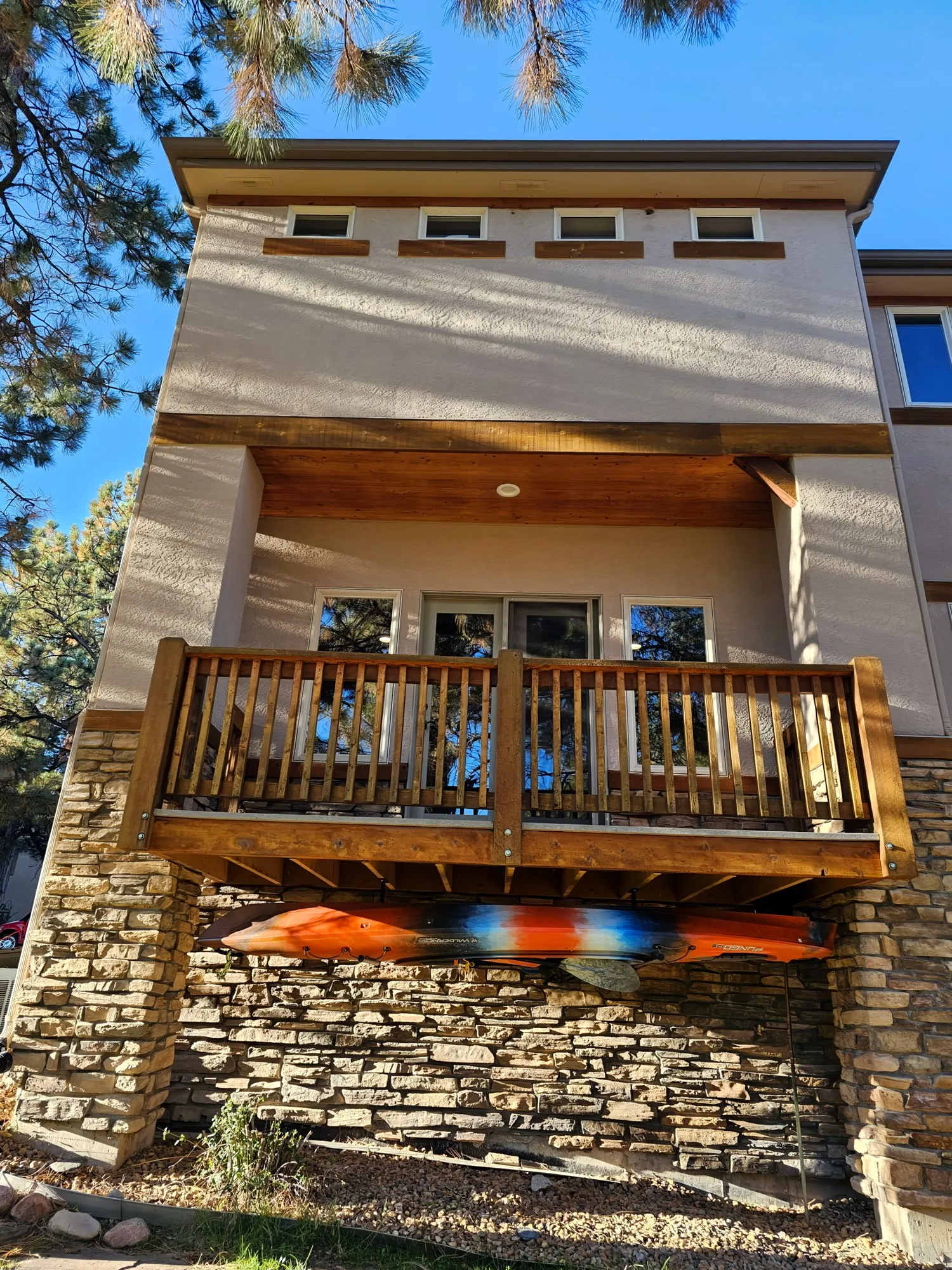 Back of a stucco home with a wood balcony and stone base
