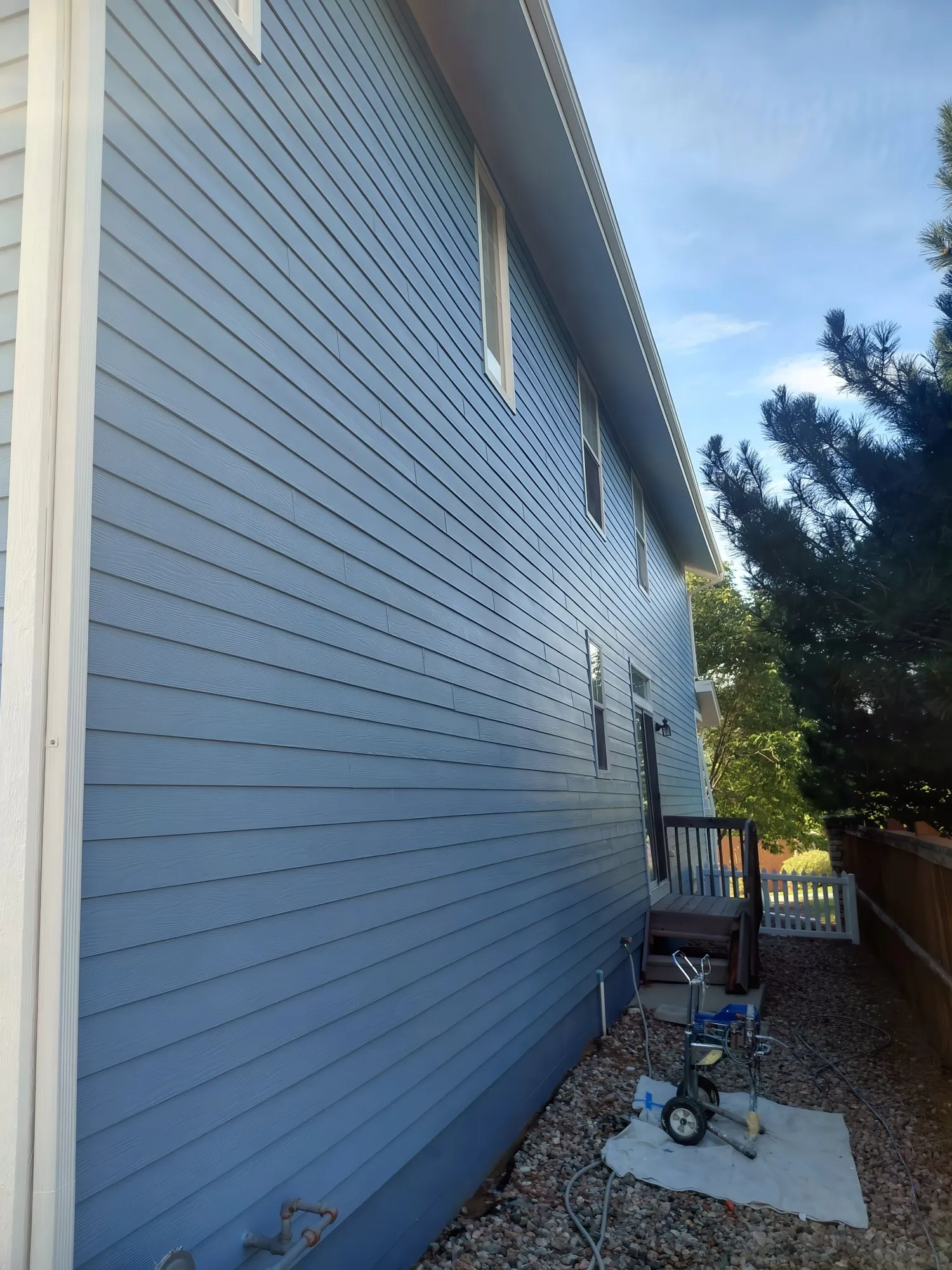 Paint sprayer on a drop cloth beside a house being painted blue