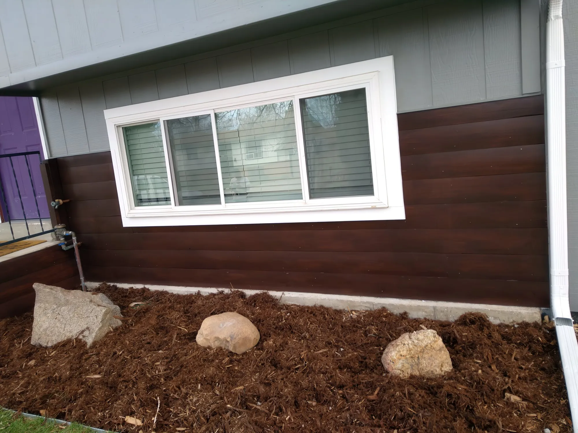 New brown lap siding installed beneath a white window with fresh mulch