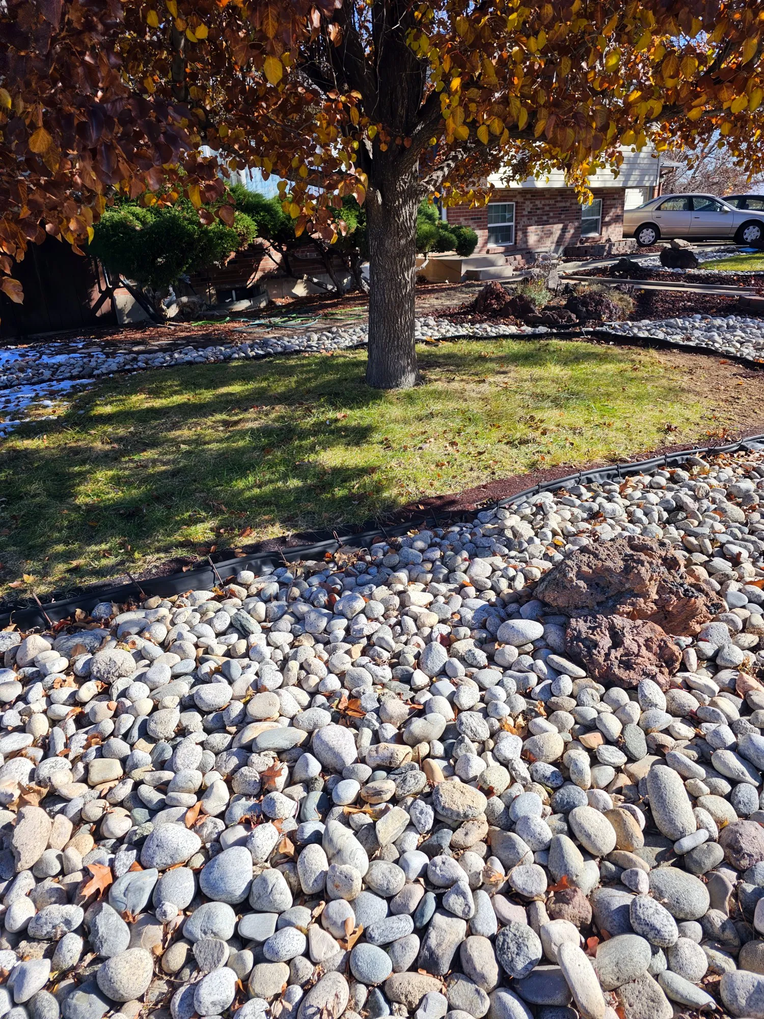 Front yard with river rock beds around a tree and green lawn